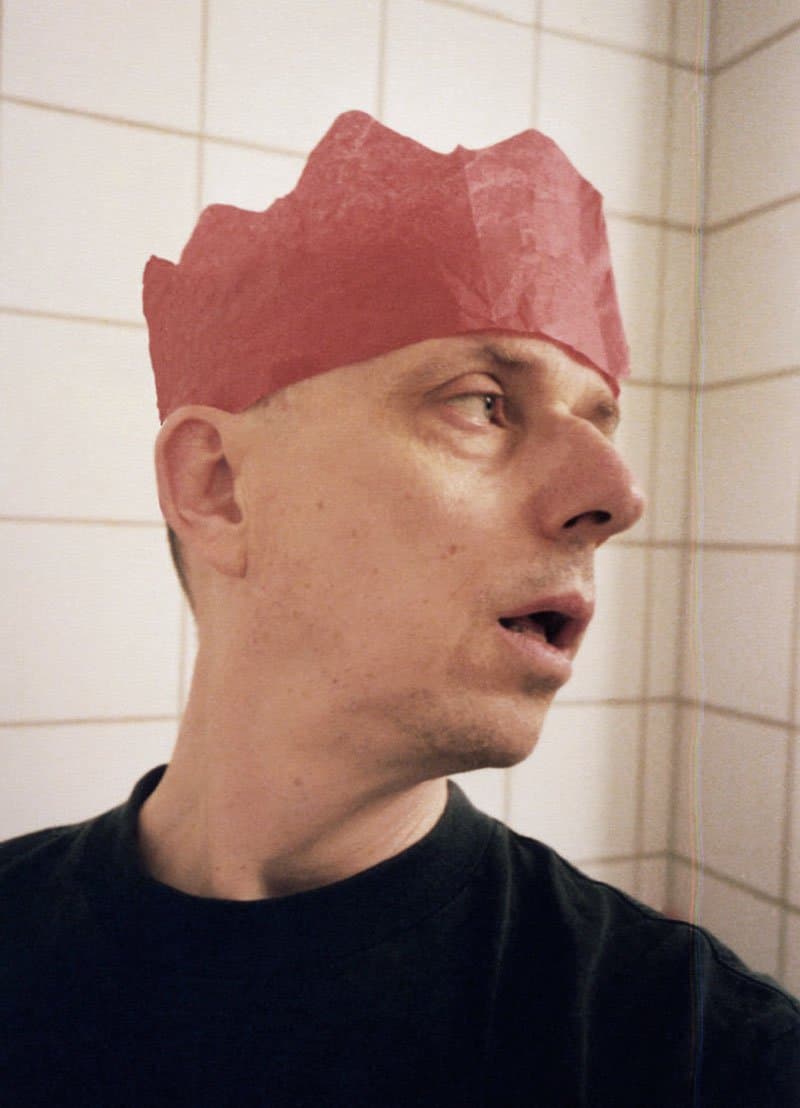 A person wearing a red paper crown is looking to the side in a tiled room.