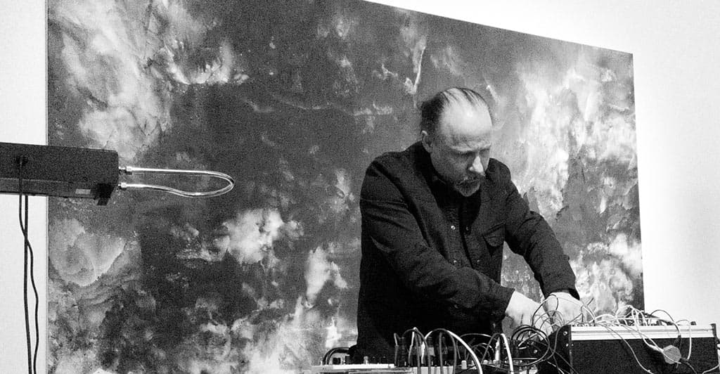 A person is manipulating wires and equipment, with a cloudy, abstract background behind them.