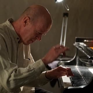 A person with a bald head is playing a piano under a desk lamp.